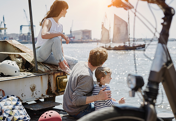 Zwei Erwachsene und ein Kind sitzen an der Elbe und schauen auf das Wasser in Hamburg.