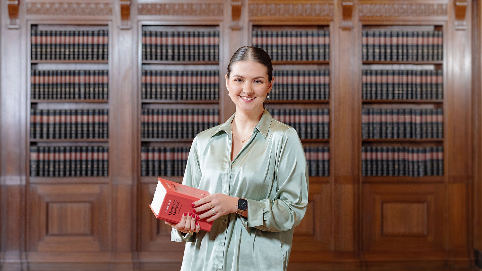 Eine Rechtspflegerin steht mit einem Gesetzbuch in einem Raum.