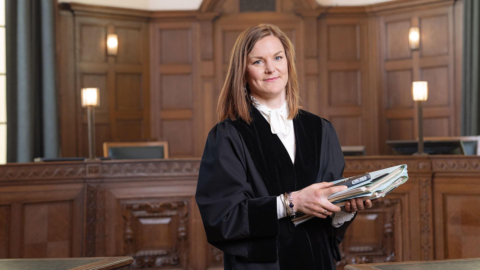 Eine Richterin steht mit Unterlagen in der Hand in einem Gerichtssaal.