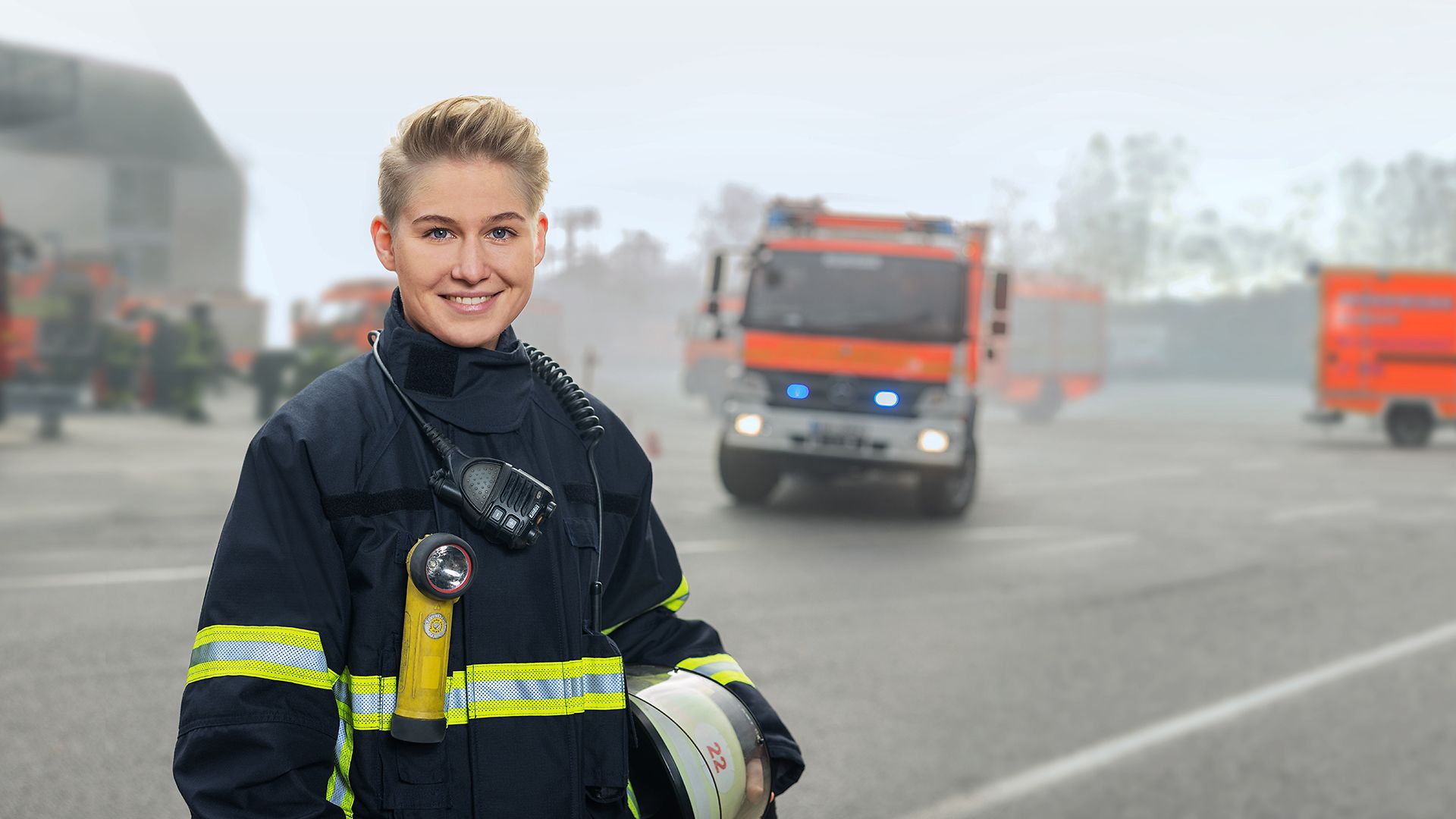 Eine Feuerwehrfrau steht vor Feuerwehrautos auf einem Platz.