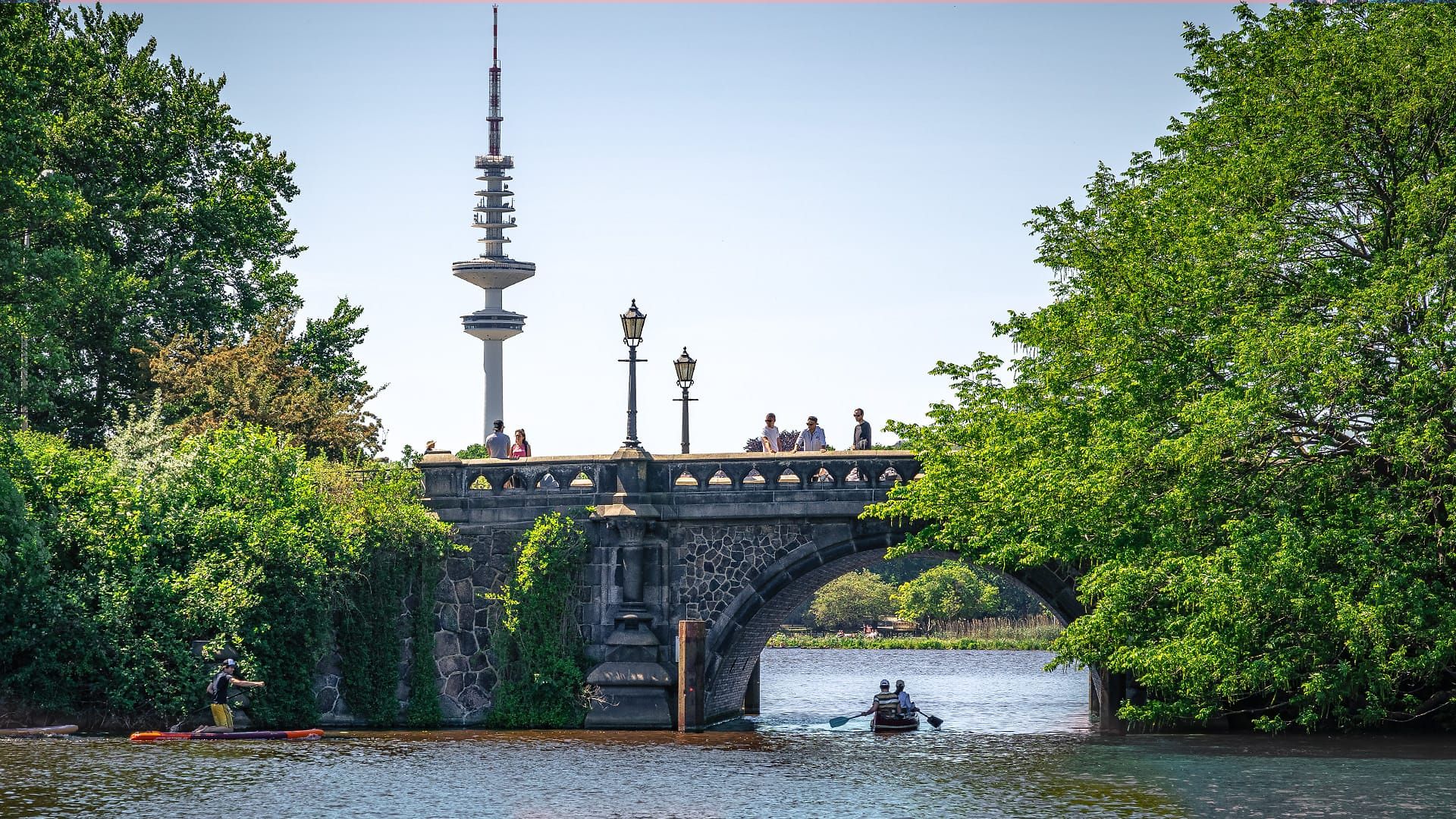 Ein Ruderboot fährt auf der Alster in Hamburg unter einer Brücke hindurch