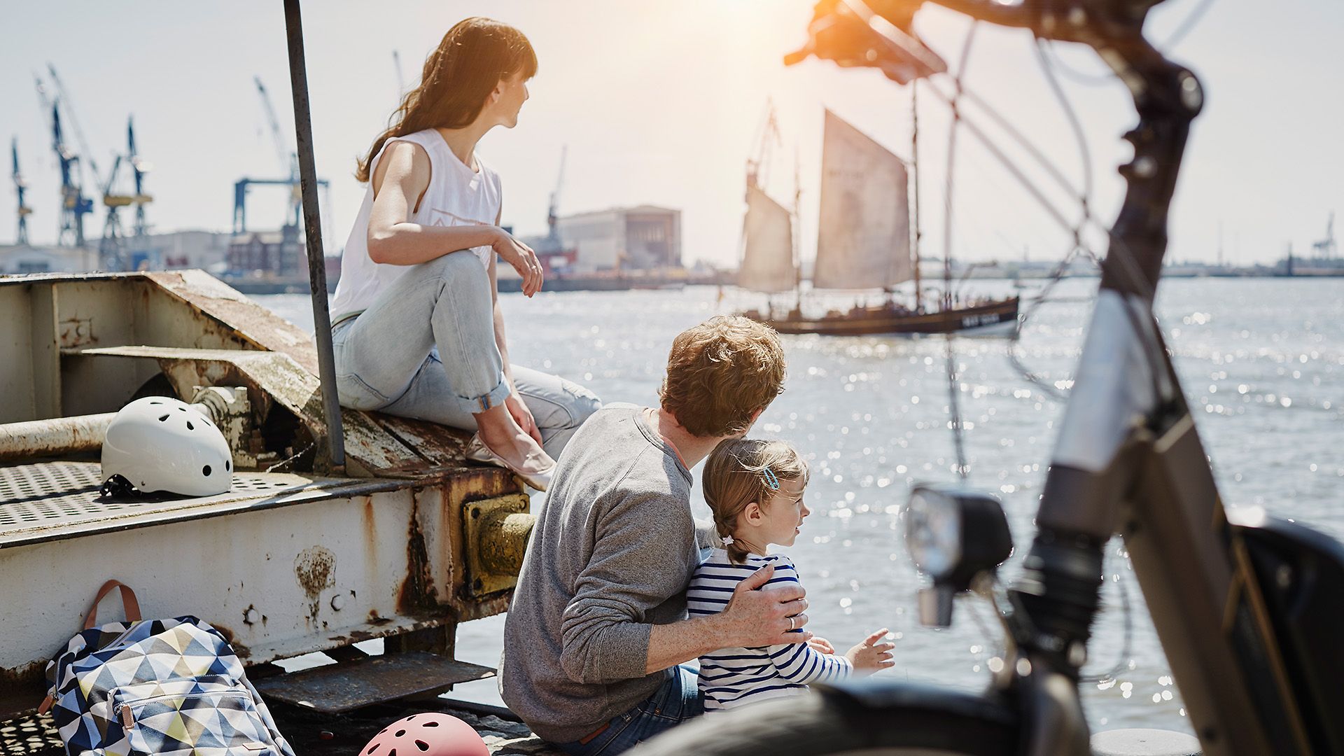 Zwei Erwachsene und ein Kind sitzen an der Elbe und schauen auf das Wasser in Hamburg.